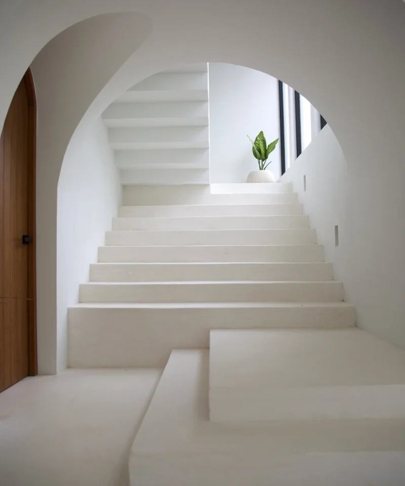 Escalera minimalista blanca con arco arquitectónico y luz natural en interior contemporáneo