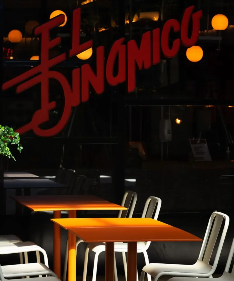 Interior de restaurante moderno con mesas de madera, sillas metálicas y rotulación en cristal