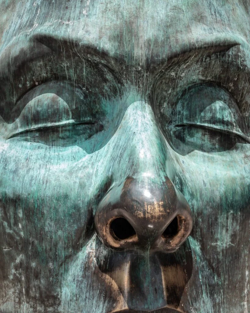 Rostro de una escultura de bronce cubierto de pátina verde